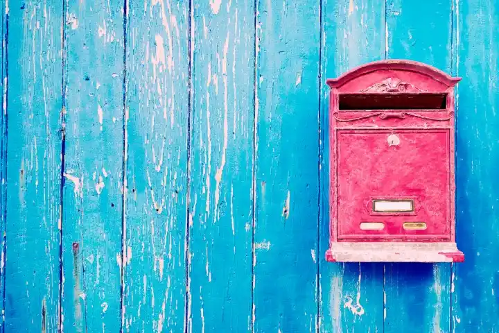 Una cassetta postale rossa &egrave; montata su una parete di legno blu usurata.