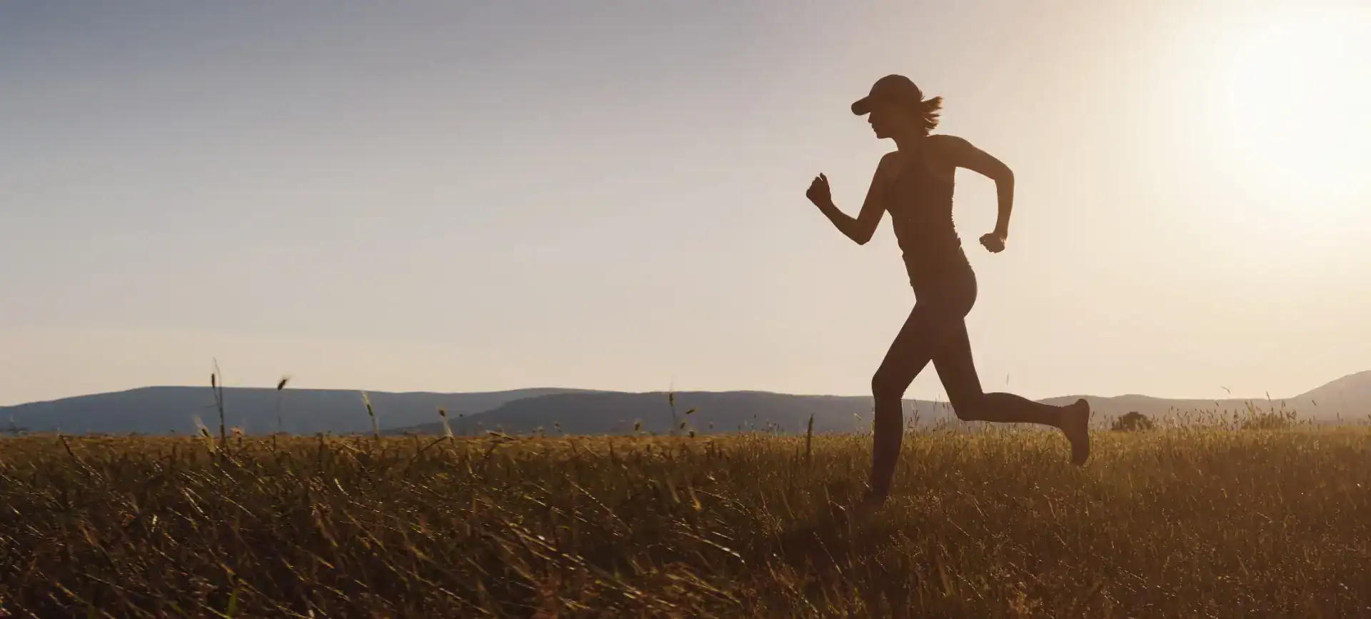 Sagoma di una persona che corre in un campo erboso al tramonto, con colline visibili sullo sfondo.